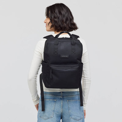 Person wearing a black backpack on a plain background