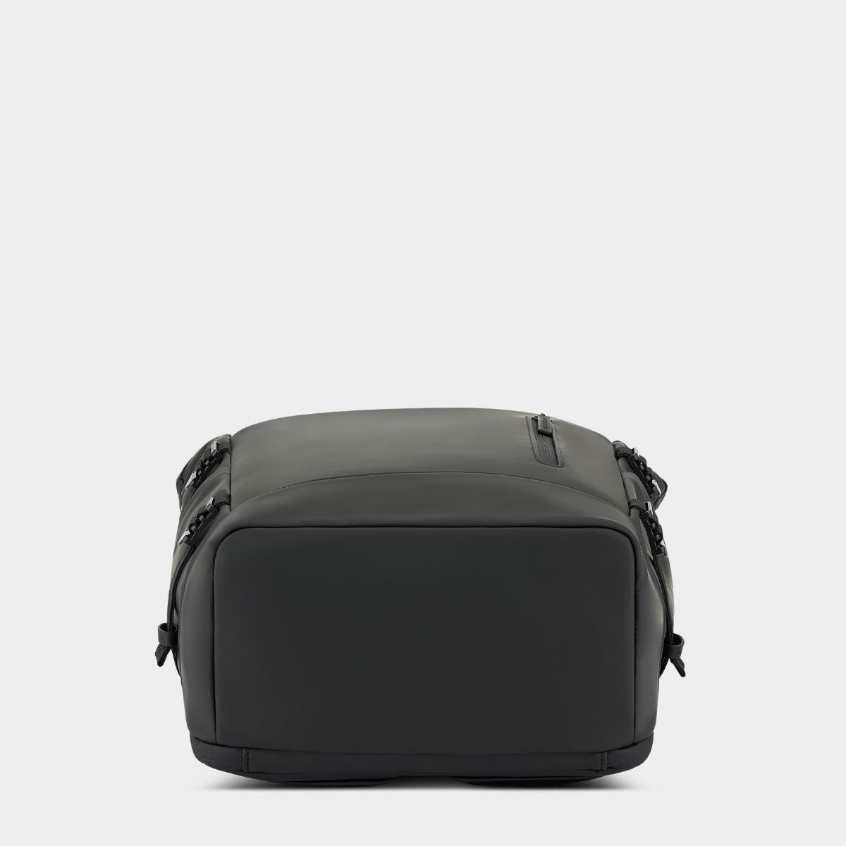 A black soft-sided backpack with a matte finish, shown from the bottom against a light gray studio background.