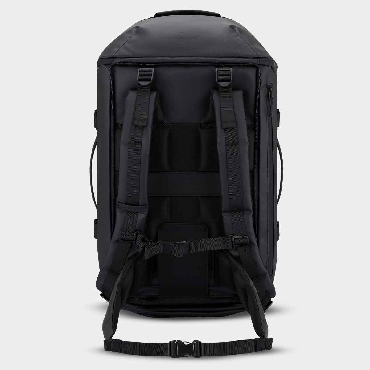 A black duffle backpack shown from the back, featuring padded shoulder straps, compression buckles, and a detachable waist strap, set against a light gray background.