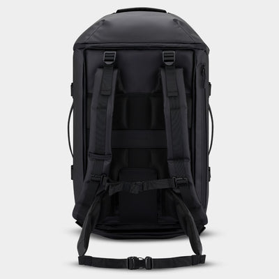 A black duffle backpack shown from the back, featuring padded shoulder straps, compression buckles, and a detachable waist strap, set against a light gray background.