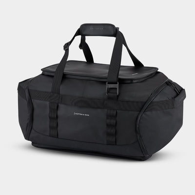 A black duffel bag with top handles, a zippered top lid, and multiple compression straps, photographed on a clean white background. The brand name 'KAPTEN & SON' is visible in white text on the front.