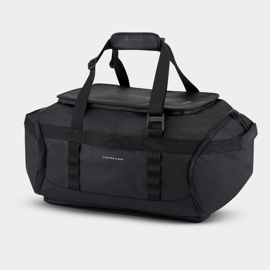 A black duffel bag with top handles, a zippered top lid, and multiple compression straps, photographed on a clean white background. The brand name 'KAPTEN & SON' is visible in white text on the front.