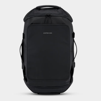 A black backpack/duffle bag with a front zippered pocket and a small white KAPTEN & SON logo on the upper left of the pocket, shown against a plain gray background.