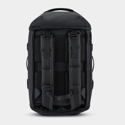 The back view of a black backpack, showing padded shoulder straps, compression buckles, and side carry loops, set against a light gray background.
