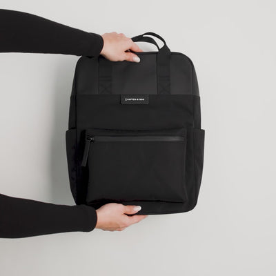Video of black backpack being unzipped from the top and packed with notebook, laptop, pens, water bottle and phone. Hands are shown packing the various items